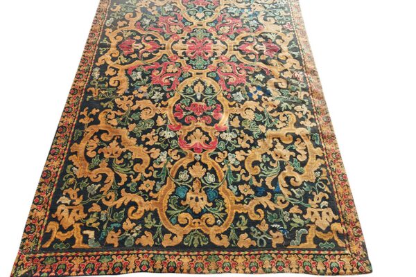 Low-pile rug with dark ground, golden baroque scrolling patterns, and bright red and green floral accents.