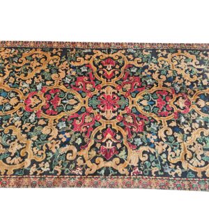 A large rug displays ornate scrolling floral patterns in gold, red, blue, and green on a dark background.