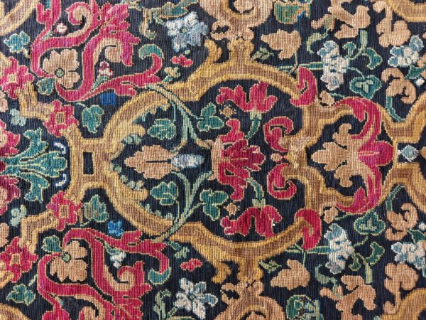 Detailed view of a low-pile rug with red, gold, and green baroque floral motifs on a navy ground.