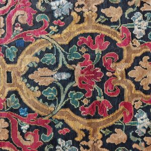 A dense, low-pile rug pattern featuring gold, crimson, teal, and light blue scrolling florals on a dark background.