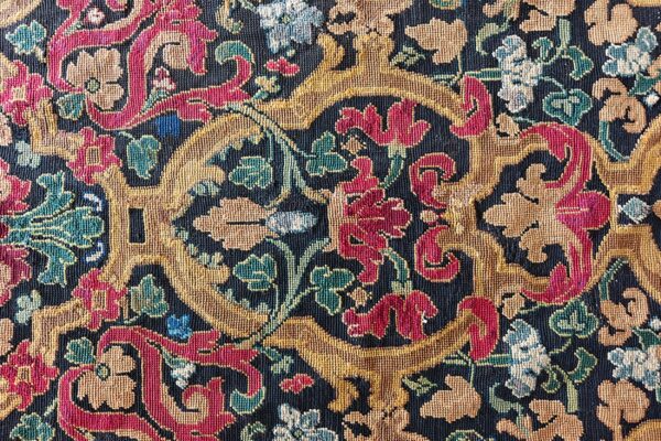 A dense, low-pile rug pattern featuring gold, crimson, teal, and light blue scrolling florals on a dark background.