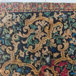 Intricate low-pile rug displaying scrolling gold and jewel-toned florals against a dark blue background.