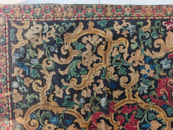 Intricate low-pile rug displaying scrolling gold and jewel-toned florals against a dark blue background.