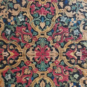 Ornate rug detail showing a navy field with crimson, gold, and green scrolling floral motifs.