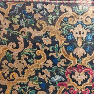Low-pile rug detail showing tan, gold, red, and blue stylized floral patterns on a dark navy field.