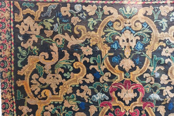 Low-pile rug detail showing tan, gold, red, and blue stylized floral patterns on a dark navy field.
