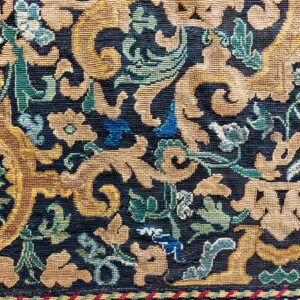 Detailed view of a dense, low-pile rug with ornate gold, blue, and green floral scrollwork on a navy background.