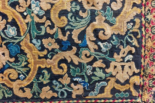 Detailed view of a dense, low-pile rug with ornate gold, blue, and green floral scrollwork on a navy background.