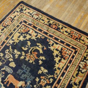 Navy rug with gold and coral stylized floral and animal patterns lies diagonally on distressed wood floor.