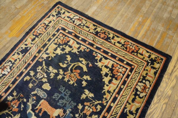 Navy rug with gold and coral stylized floral and animal patterns lies diagonally on distressed wood floor.