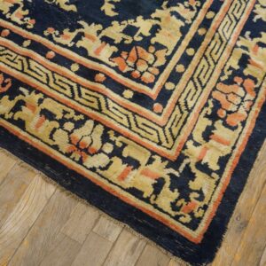 The rug border, featuring yellow geometric and coral floral motifs on navy blue, lies on light wood floors.