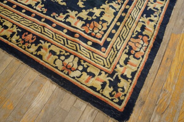 The rug border, featuring yellow geometric and coral floral motifs on navy blue, lies on light wood floors.