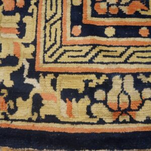 Textured navy rug corner showing borders in beige and coral geometric and abstract patterns on wood flooring.