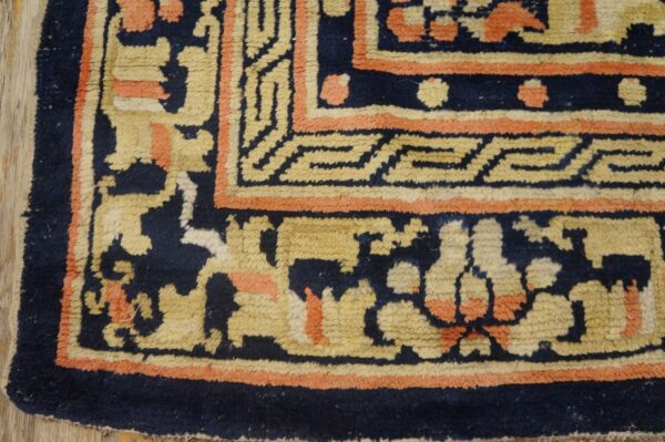 Textured navy rug corner showing borders in beige and coral geometric and abstract patterns on wood flooring.