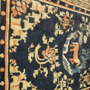 Detail of a dark blue rug showing gold, orange, and light blue floral patterns and geometric borders.