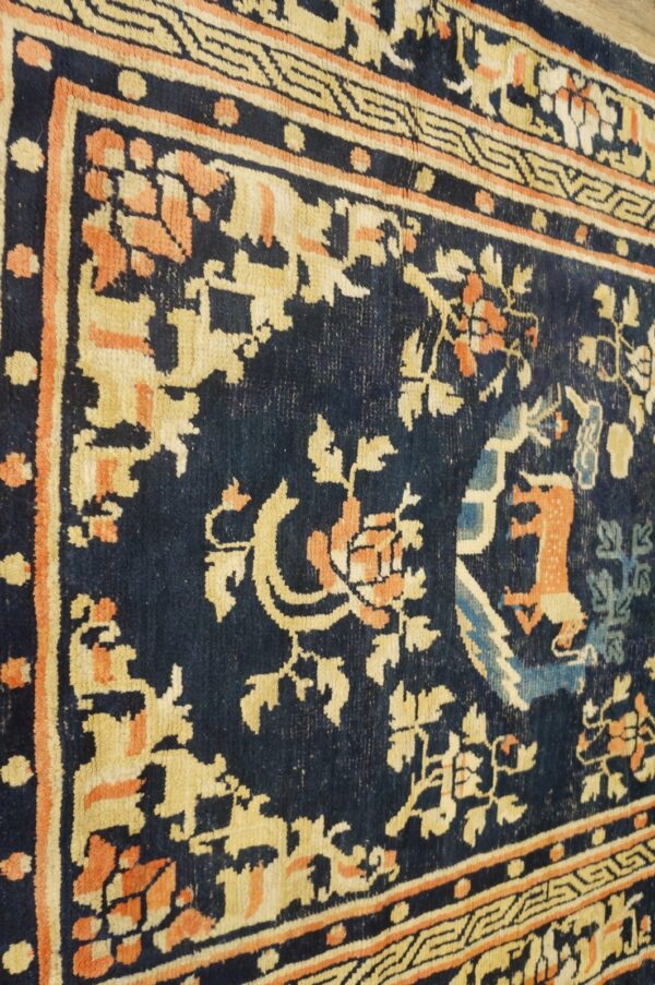 Detail of a dark blue rug showing gold, orange, and light blue floral patterns and geometric borders.