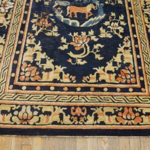 Navy blue rug with intricate gold and orange motifs and borders rests on light wood floorboards.
