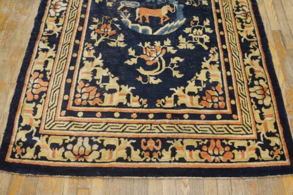 Navy blue rug with intricate gold and orange motifs and borders rests on light wood floorboards.