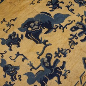 Tan rug with dense dark blue stylized creature patterns and a partially visible border stripe.