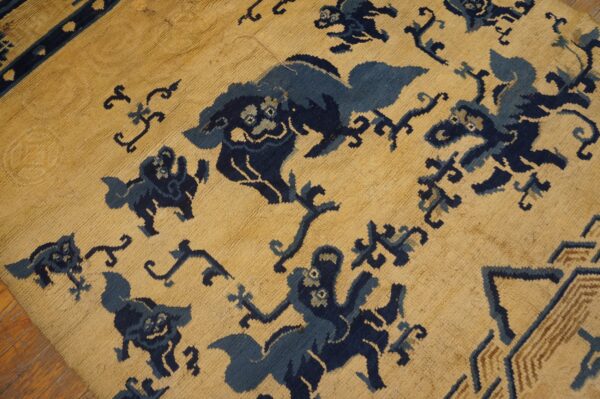 Tan rug with dense dark blue stylized creature patterns and a partially visible border stripe.