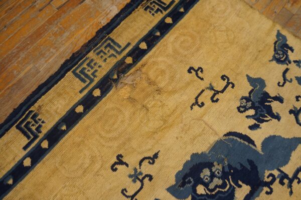 Worn yellow rug with dark blue mythological figures and geometric border on distressed wood floor.