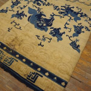 Yellow rug with stylized dark blue figures and a geometric border rests on worn wood flooring.