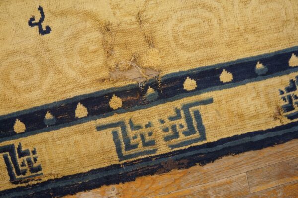 Close-up of a damaged yellow high-pile rug with dark blue geometric patterns lying on wood flooring.
