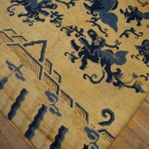 Low-pile yellow rug with navy blue mythical creatures and a tan geometric border rests on wood flooring.