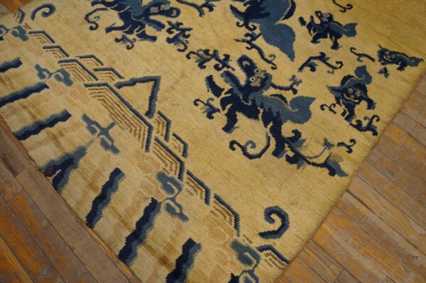 Low-pile yellow rug with navy blue mythical creatures and a tan geometric border rests on wood flooring.