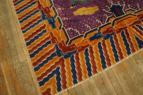 Purple rug with yellow clouds and geometric orange, blue, and red border on wood planks.