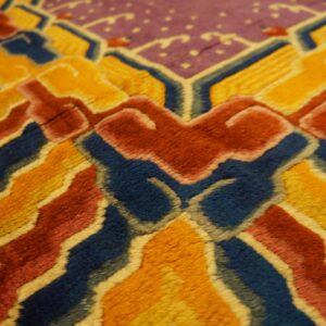 Highly textured rug close-up with bold geometric patterns in deep blue, gold, reddish-orange, and purple.