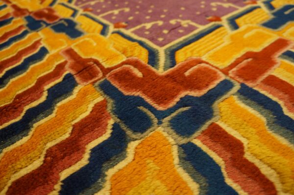 Highly textured rug close-up with bold geometric patterns in deep blue, gold, reddish-orange, and purple.