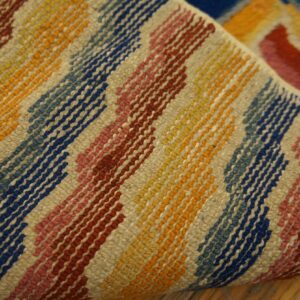 Textured rug detail showing diagonal stripes of vibrant blue, yellow, red, and beige resting on a wood floor.