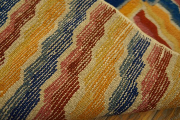 Textured rug detail showing diagonal stripes of vibrant blue, yellow, red, and beige resting on a wood floor.