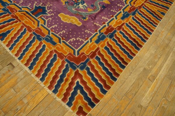 Purple rug with a blue dragon pattern and geometric borders in blue, orange, and red resting on wood flooring.