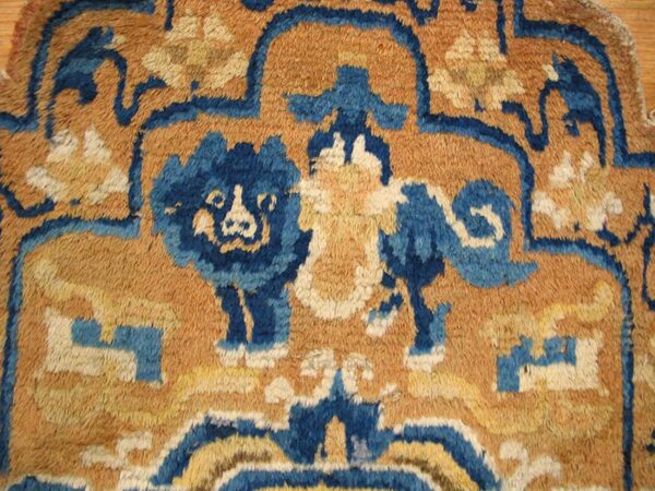 Coarse, shaggy pile rug detail showing a stylized dark blue and cream pattern on a golden tan ground.