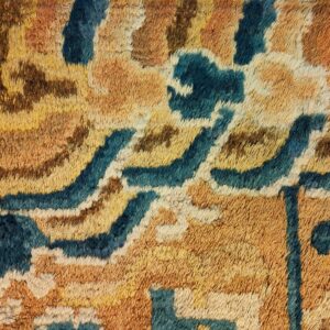 Textured high-pile rug detail with abstract organic shapes in teal, amber, gold, and dark brown.