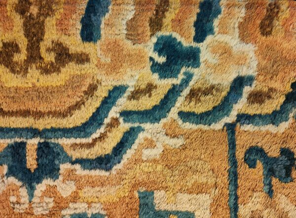 Textured high-pile rug detail with abstract organic shapes in teal, amber, gold, and dark brown.