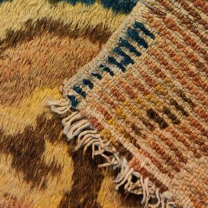 Close-up showing the shaggy, multi-color patterned rug face folded over its flatwoven backing with visible fringe.