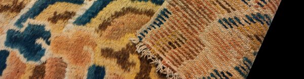 Close-up showing the shaggy, multi-color patterned rug face folded over its flatwoven backing with visible fringe.
