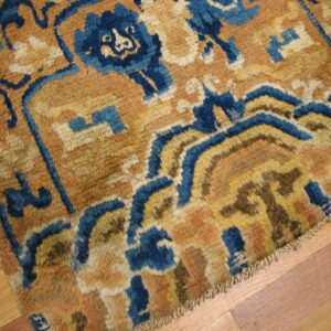 Heavily textured rug with abstract blue and golden-brown designs rests on a light hardwood floor.