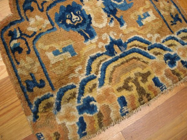Heavily textured rug with abstract blue and golden-brown designs rests on a light hardwood floor.