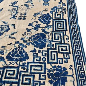 Cream rug with blue floral and stylized vase motifs, bordered by geometric square spiral patterns.