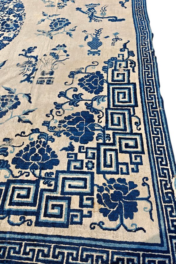 Cream rug with blue floral and stylized vase motifs, bordered by geometric square spiral patterns.