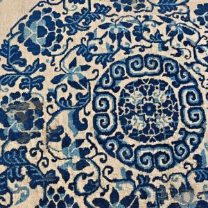 Detail shot of a rug with indigo and sky blue scrolling florals and a center medallion on cream pile.