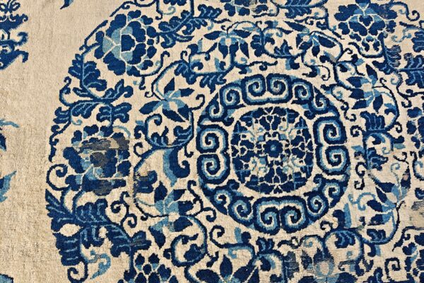 Detail shot of a rug with indigo and sky blue scrolling florals and a center medallion on cream pile.