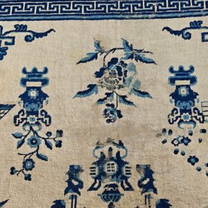 Detailed view of a cream rug with dark blue traditional patterns, including floral elements and a meander border.