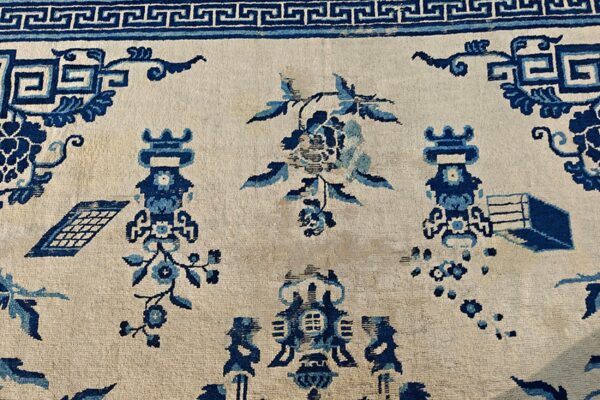 Detailed view of a cream rug with dark blue traditional patterns, including floral elements and a meander border.