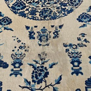 Low-pile rug detail showing scattered blue flowers and stylized vessels on a light cream field.