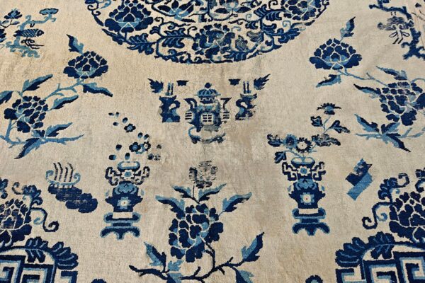 Low-pile rug detail showing scattered blue flowers and stylized vessels on a light cream field.